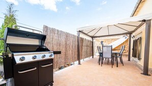 Un patio exterior con una parrilla, una mesa con sillas y un área de estar techada.