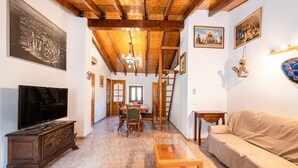 Una habitación con techo de madera, televisión, sofá, mesa de comedor con sillas y candelabro.