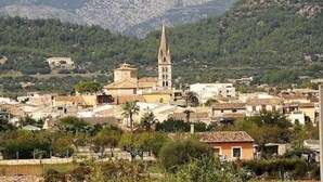 Un pueblo con una imponente torre de iglesia, rodeado de edificios residenciales y vegetación.