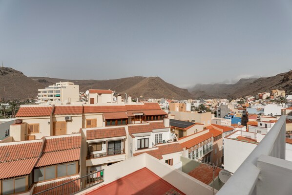 Zona residencial con edificios de tejados de teja y cielo despejado, con montañas al fondo.