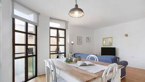 A dining area with a wooden table, white chairs, a blue sofa, and a TV. - Vacation Home 'Casa Brando' with Balcony and Wi-Fi (Corralejo)