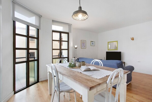 A dining area with a wooden table, white chairs, a blue sofa, and a TV.