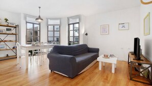 A modern living room with a grey sofa, a white dining table, and a TV on a wooden stand. - Vacation Home 'Casa Brando' with Balcony and Wi-Fi (Corralejo)