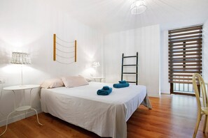 Un dormitorio con cama, mesitas de noche, lámpara, silla y ventana con persianas.