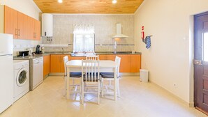 Una cucina compatta con mobili in legno, una lavatrice integrata, un tavolo da pranzo con sedie e una finestra con tende.