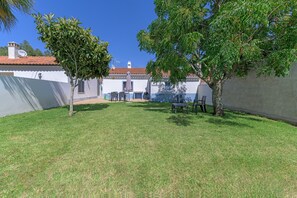 Une cour avec un bâtiment blanc, un arbre et du mobilier d’extérieur.