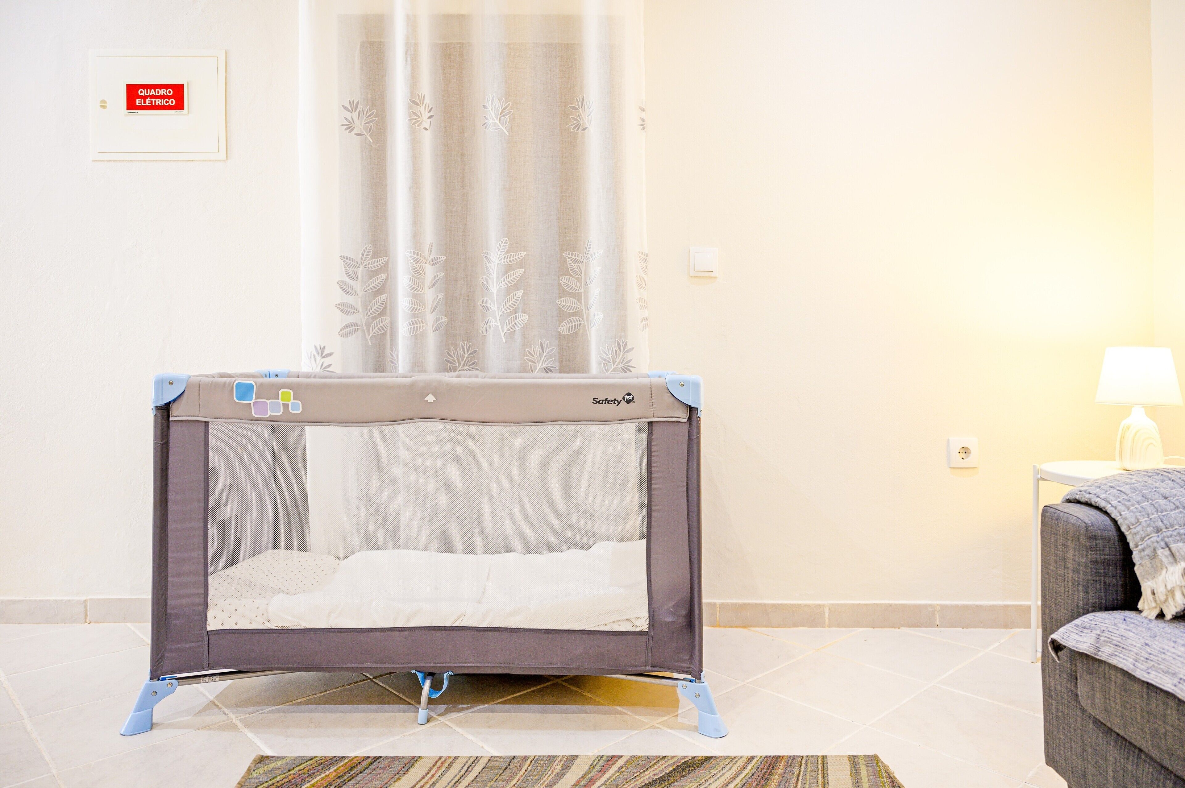 Una habitación con un corralito de seguridad para bebés, un sofá, una lámpara y suelo de baldosas.
