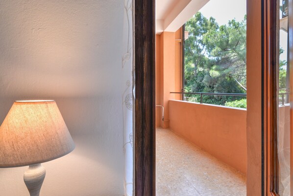Une pièce avec une lampe, un balcon avec une balustrade et une vue sur les arbres.