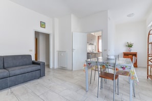 Un soggiorno moderno con un divano grigio, un tavolo da pranzo con sedie e una cucina sullo sfondo.