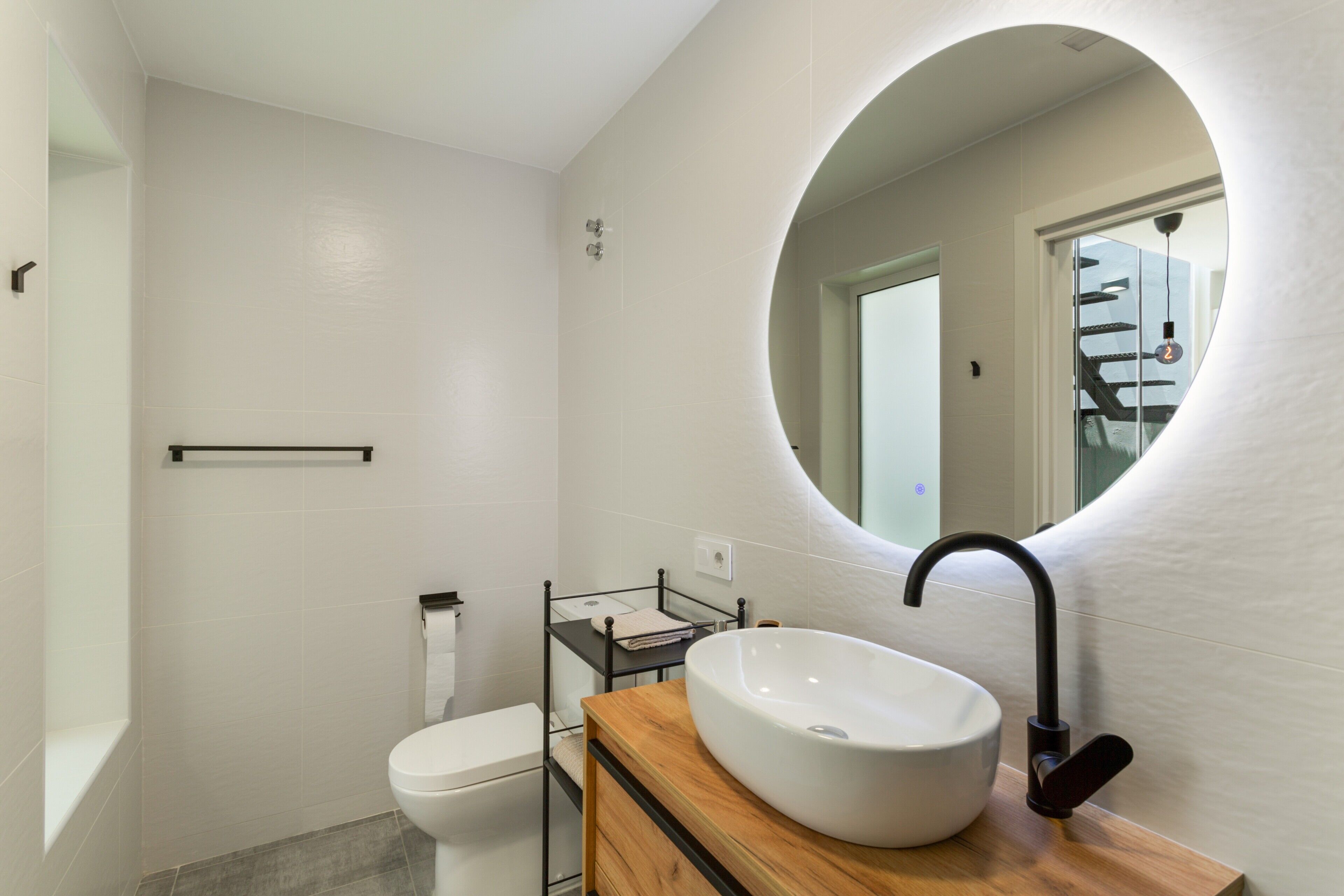 Un baño moderno con lavamanos blanco, grifo negro y tocador de madera.