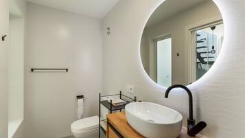 Un baño moderno con lavamanos blanco, grifo negro y tocador de madera.
