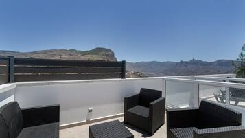 Terraza en la azotea con mobiliario de mimbre y vistas a montañas.