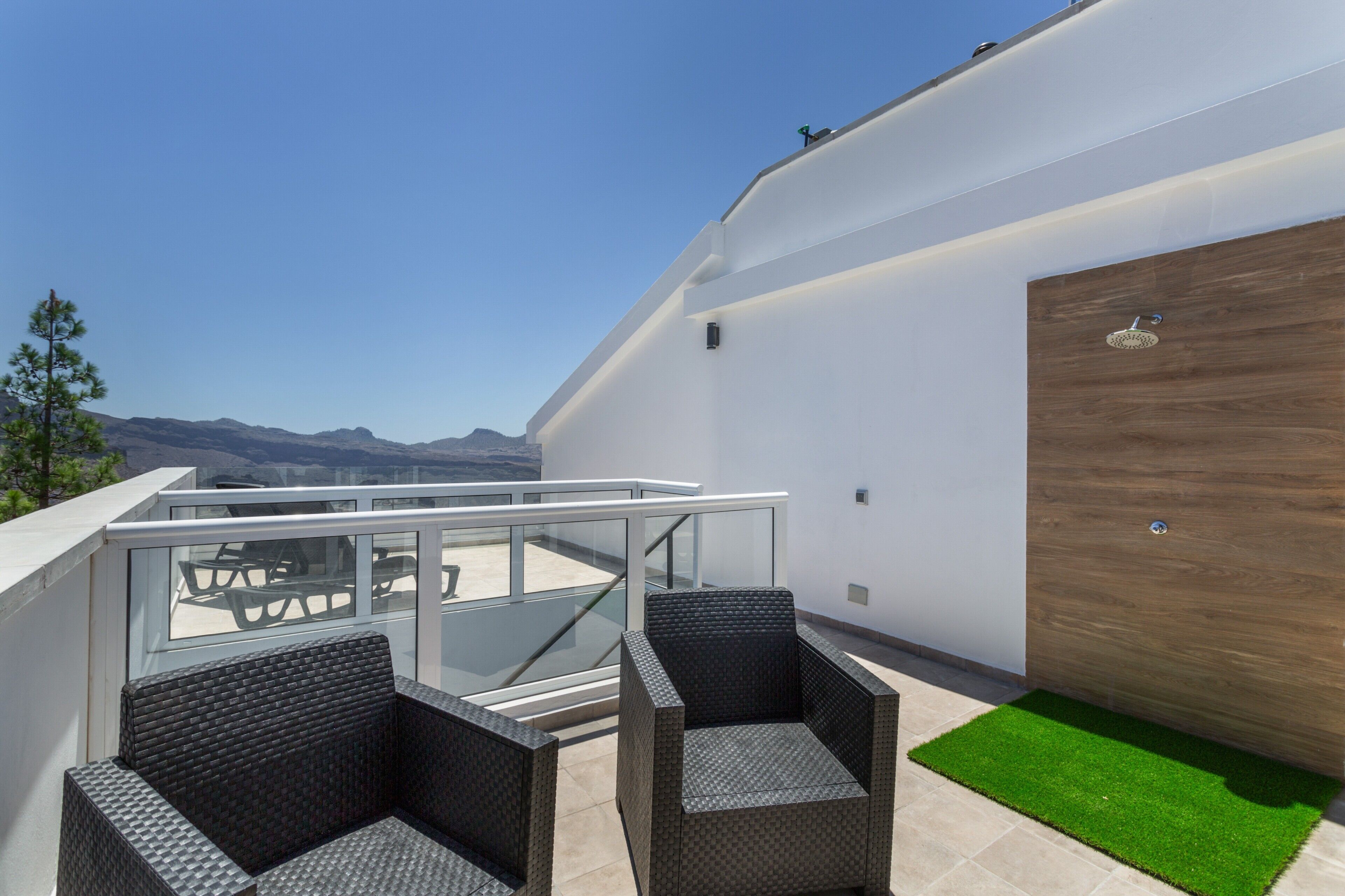 Un balcone con mobili in vimini, ringhiera in vetro e vista sulle montagne.