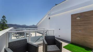 Un balcone con mobili in vimini, ringhiera in vetro e vista sulle montagne.