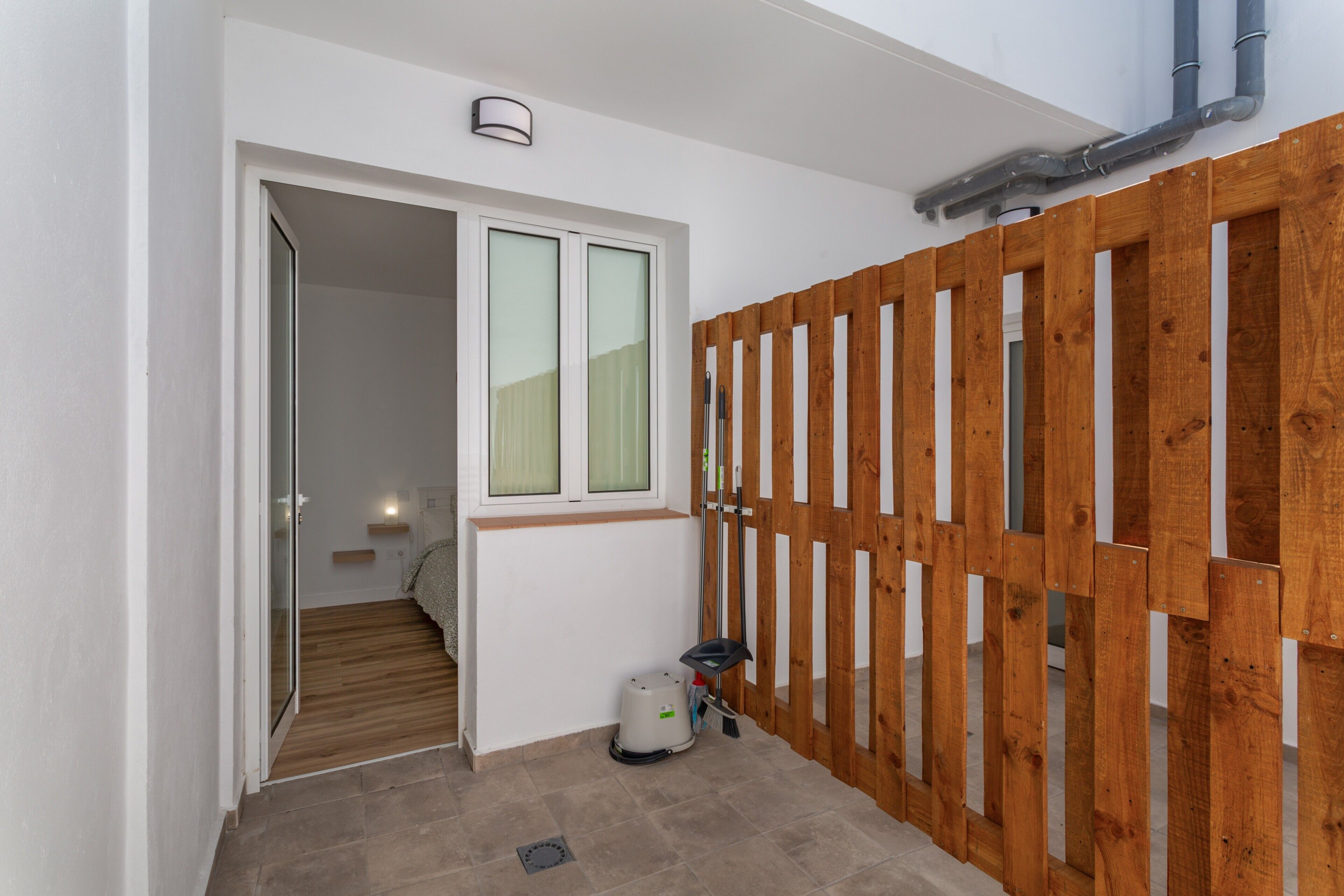 Un passadís amb una separació de fusta, una finestra amb vidre mat, un aspirador i una escala que condueix a una altra habitació.