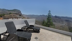 Un balcón con dos sillones de descanso y una mesa, con vistas a un paisaje montañoso.