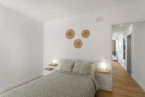 Ein Schlafzimmer mit Bett, Nachttischen, Wanddekoration und einem zur anderen Kammer führenden Flur.