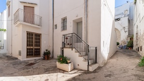A narrow street with a white building featuring a balcony, a door with a window, and a small staircase. - Apartment 'Elena Inn' with Private Terrace, Wi-Fi and Air Conditioning (Matino)