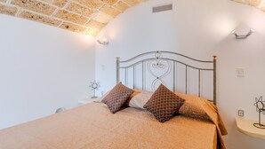 A bedroom with a brick ceiling, a metal bed frame, patterned bedding, and a small bedside table with a lamp. - Apartment 'Elena Inn' with Private Terrace, Wi-Fi and Air Conditioning (Matino)