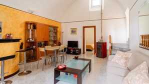 A living room with a sofa, a glass coffee table, a TV, a dining area with a table and chairs, and a kitchen area with cabinets and a refrigerator. - Apartment 'Elena Inn' with Private Terrace, Wi-Fi and Air Conditioning (Matino)