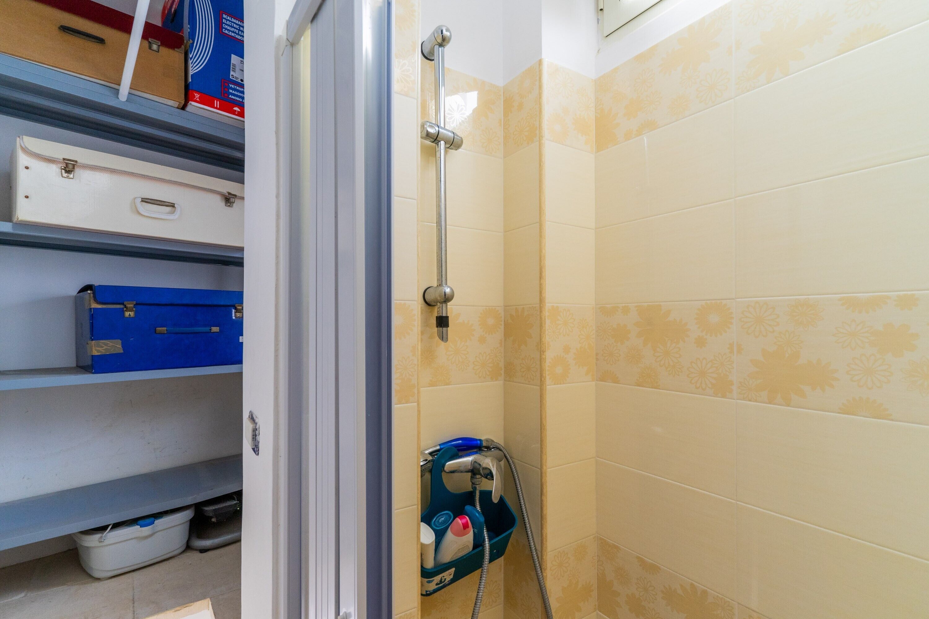 A bathroom with a shower, tiled walls, and storage shelves with suitcases.