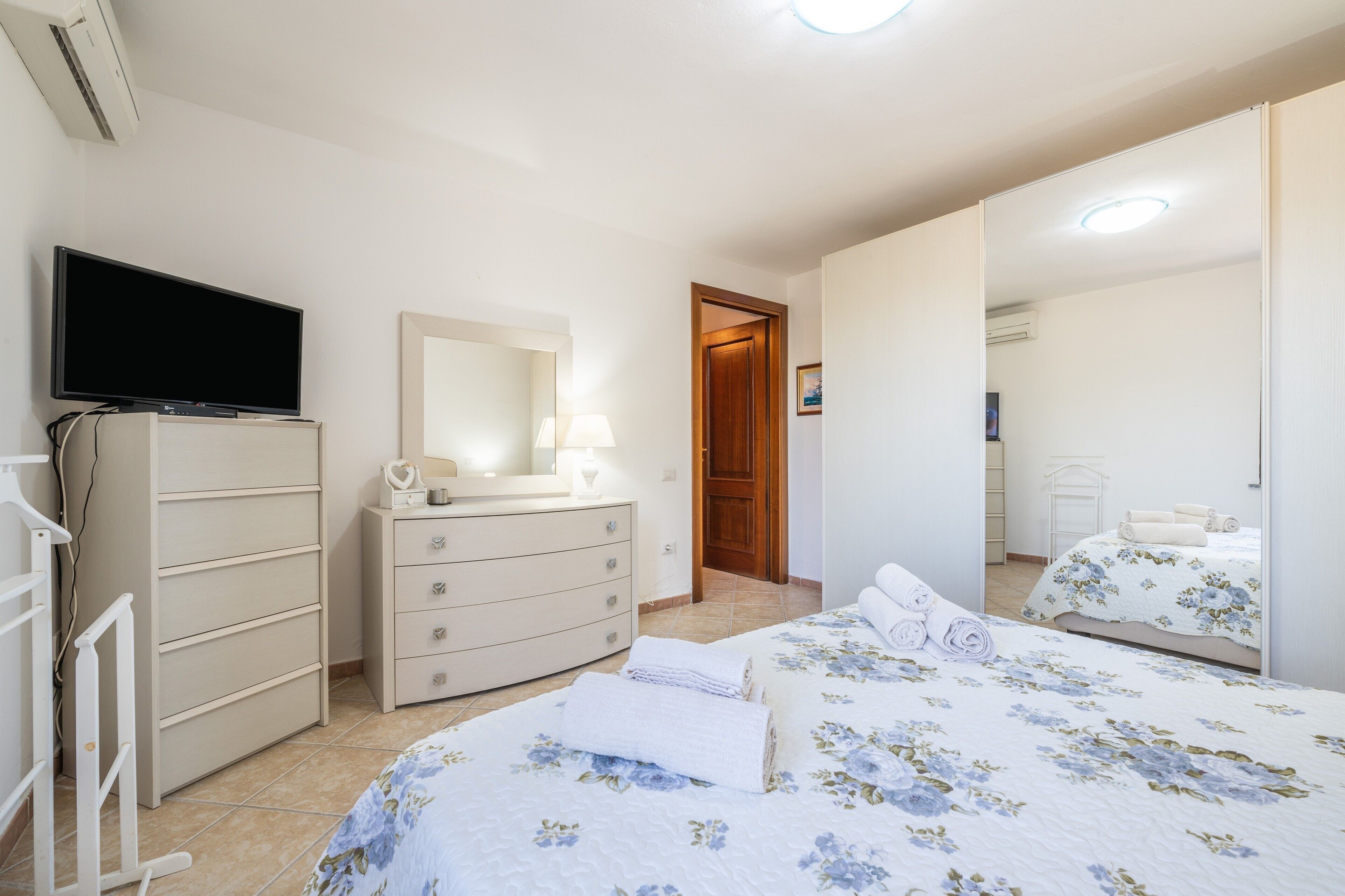 A bedroom with a TV, dresser, two beds, and a mirror.