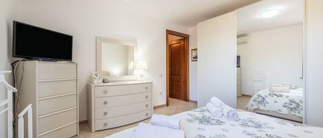 A bedroom with a TV, dresser, two beds, and a mirror.