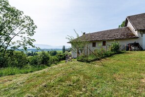 Ein ländliches Haus mit geneigtem Dach, umgeben von Grün und einer hügeligen Landschaft.