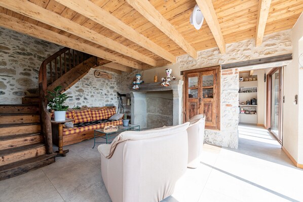 A rustic interior with a stone wall, wooden staircase, a sofa, and a dining table. - Bed and breakfast "Chambre Bleue" with Mountain View, Private Terrace and Shared Garden (Moye)