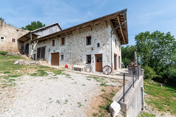 A stone building with a sloped roof, a gravel driveway, and a fenced area. - Bed and breakfast "Chambre Bleue" with Mountain View, Private Terrace and Shared Garden (Moye)