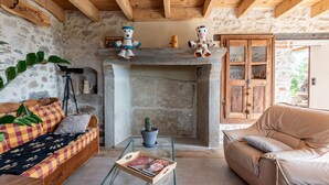 A rustic interior with a stone fireplace, wooden beams, a sofa with patterned cushions, a glass coffee table, and a door with glass panels. - Bed and breakfast "Chambre Bleue" with Mountain View, Private Terrace and Shared Garden (Moye)