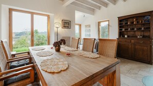 Een eetgedeelte met een grote houten tafel, rieten stoelen en uitzicht op de omgeving.
