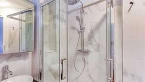 Ein modernes Badezimmer mit einer gläsernen Duschkabine, einer Marmorwand und einem Waschbecken mit Marmorplatte.