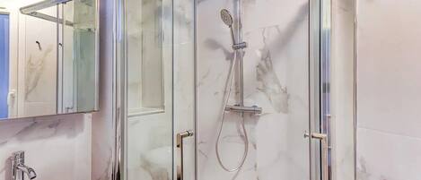 Un bany modern amb dutxa tancada per vidre, paret amb mosaic de marbre i un lavabo amb taulell de marbre.