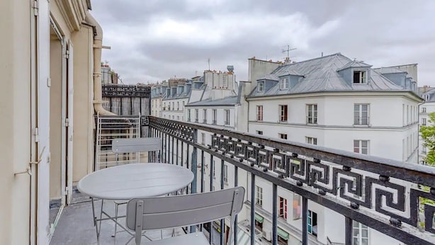 Ein Balkon mit Tisch und Stühlen, der auf eine Reihe von Gebäuden mit klassischer europäischer Architektur blickt.