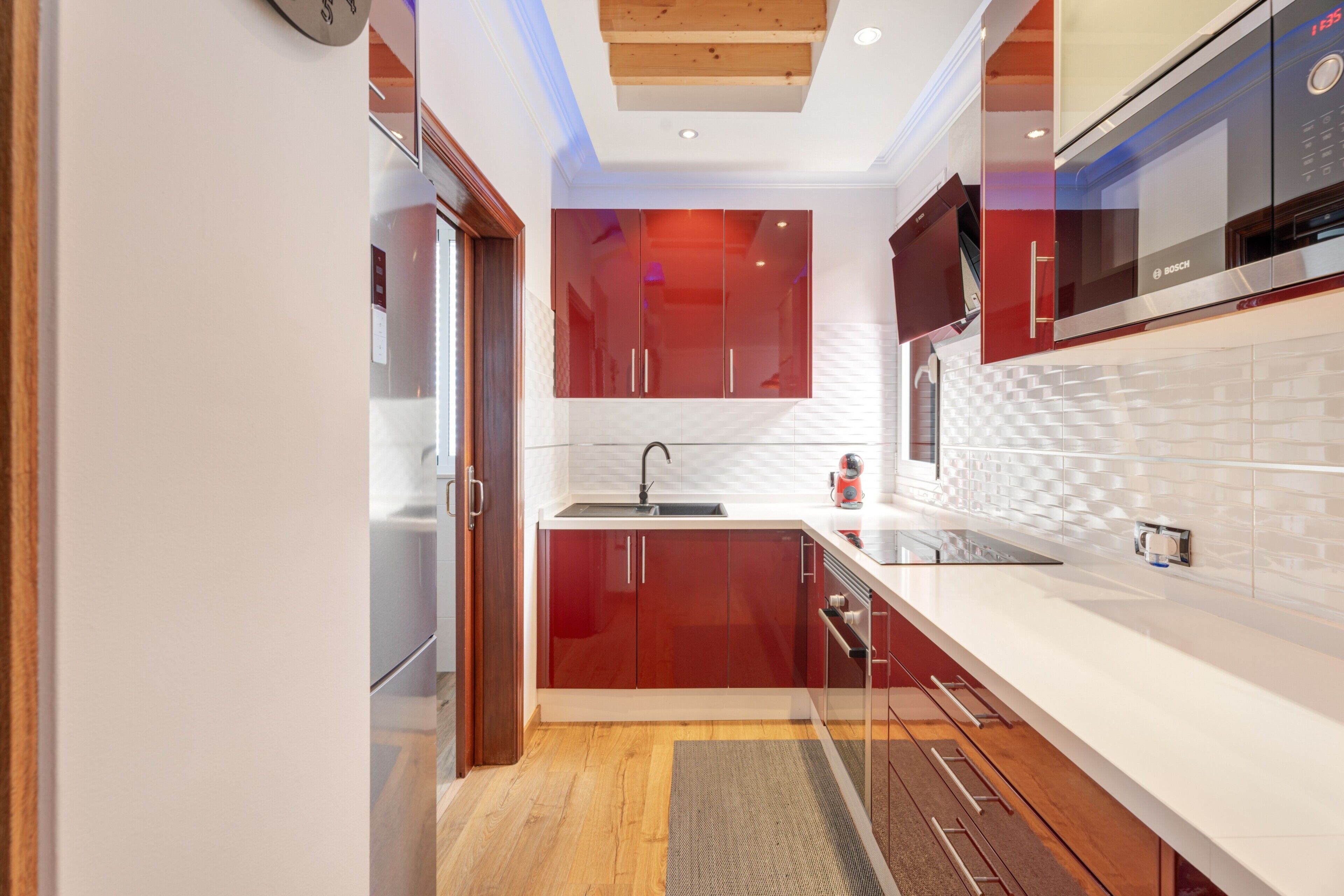 Une cuisine moderne avec des meubles rouges, un plan de travail blanc et un four Bosch.