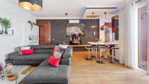 Una sala de estar moderna con un sofá seccional gris, un comedor con taburetes altos y una cocina con salpicadero de piedra.