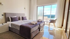 Ein modernes Schlafzimmer mit einem großen Bett, einem Nachttisch, einem Sessel und Blick ins Freie.