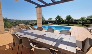 Um pátio externo com piscina, rodeado por cadeiras e uma mesa.