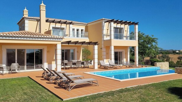 Ein zweistöckiges Haus mit Swimmingpool, Sitzgelegenheiten im Freien und einem Garten.