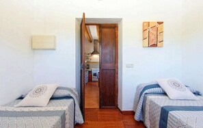 A room with two beds, a wooden door, a kitchen in the background, and a wall-mounted light fixture. - Villa 'Sa Cova' with Private Pool, Wi-Fi and Air Conditioning (Illes Balears)