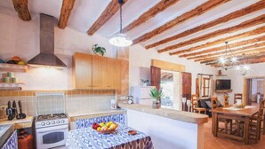 A kitchen with a gas stove, oven, and a dining area with a table set for two. - Villa 'Sa Cova' with Private Pool, Wi-Fi and Air Conditioning (Illes Balears)