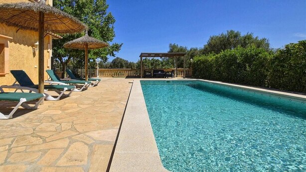A swimming pool with lounge chairs and umbrellas, surrounded by greenery. - Villa 'Sa Cova' with Private Pool, Wi-Fi and Air Conditioning (Illes Balears)