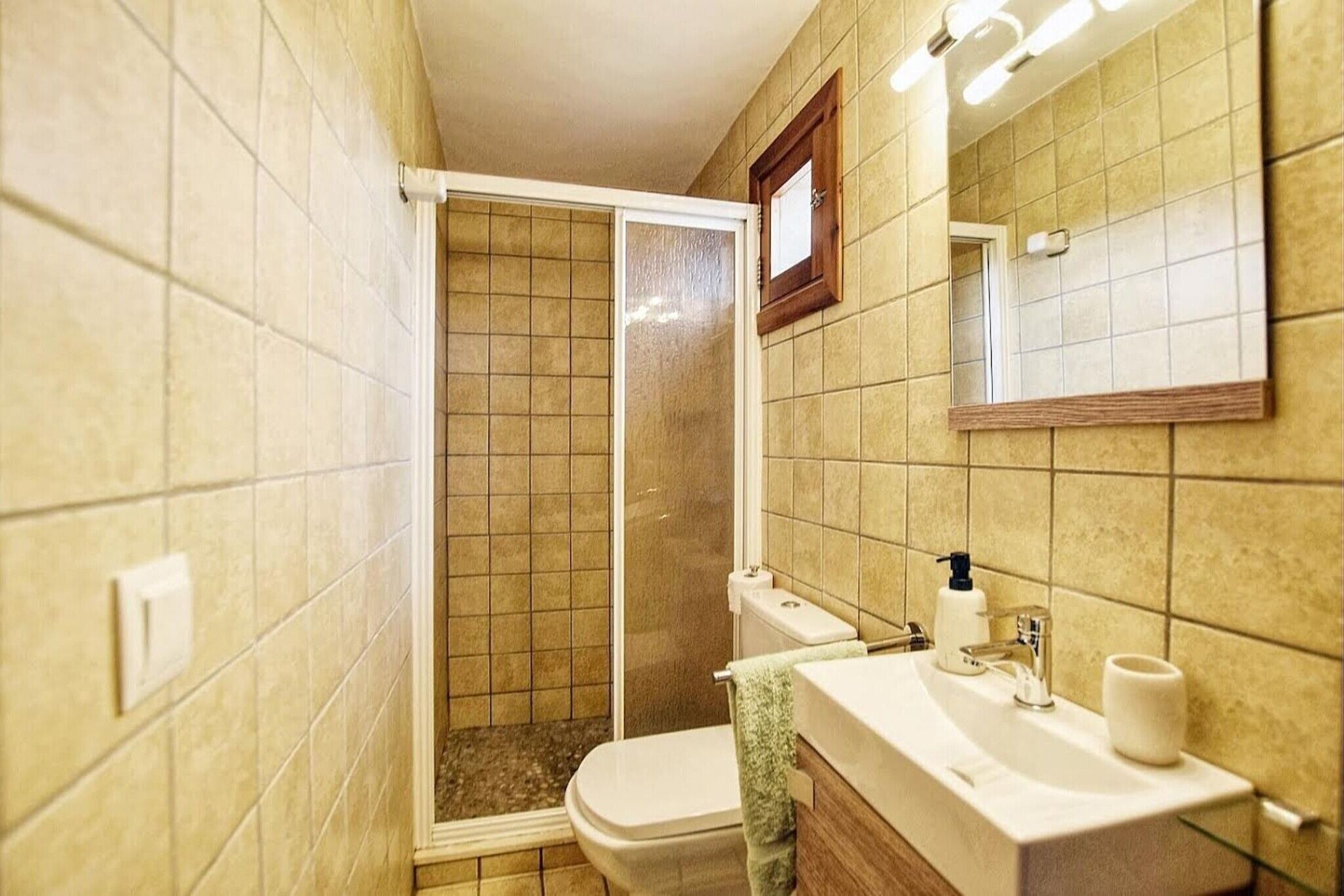 Een badkamer met douche, toilet, wastafel en spiegel.