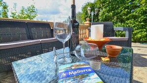 An outdoor seating area with a table, a wine bottle, glasses, a candle, and a travel guide book. - Villa 'Sa Cova' with Private Pool, Wi-Fi and Air Conditioning (Illes Balears)