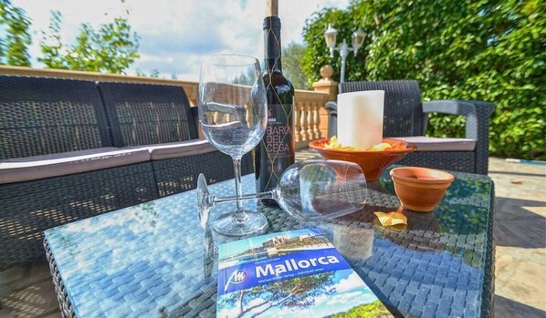 An outdoor seating area with a table, a wine bottle, glasses, a candle, and a travel guide book. - Villa 'Sa Cova' with Private Pool, Wi-Fi and Air Conditioning (Illes Balears)