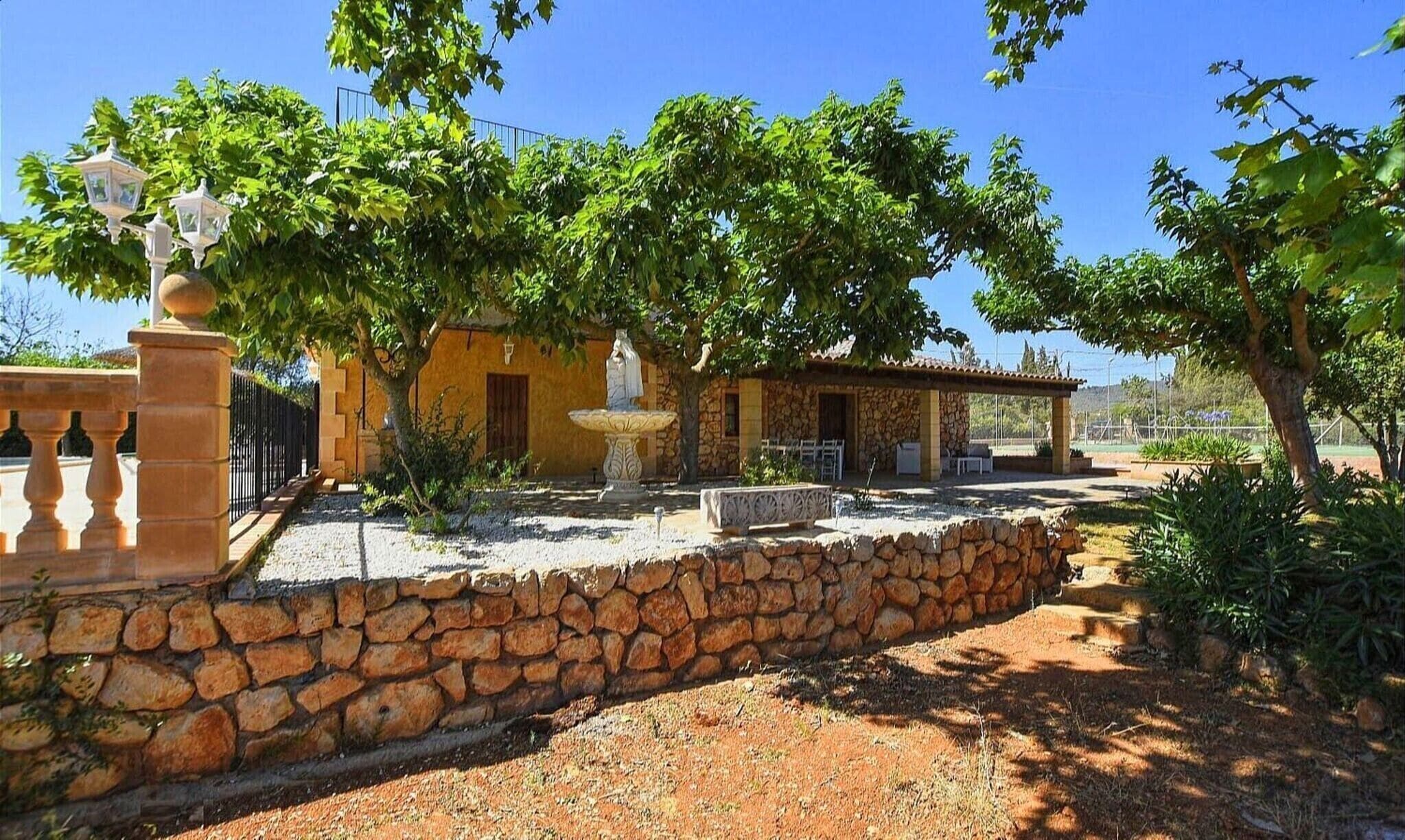 A stone wall, a yellow building, and a pergola with a statue.