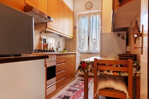 A kitchen with wooden cabinets, a refrigerator, a stove, and a dining table with a floral tablecloth.