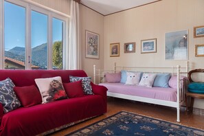 A room with a red sofa, a white bed, and a view of mountains through large windows.