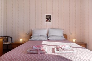 A neatly made bed with two pillows, a bedside table with a lamp, and a framed picture on the wall.